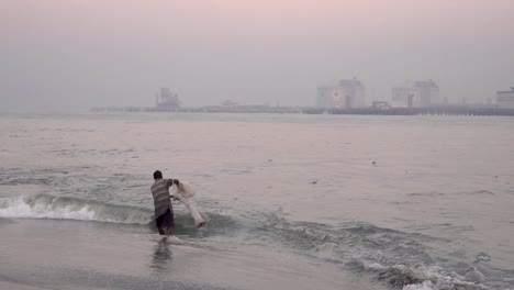 Slow-motion-of-waves-coming-in-to-sandy-beach-coastline-as-Fort-Cochin-fisherman-spins-to-throw-his-net-into-water