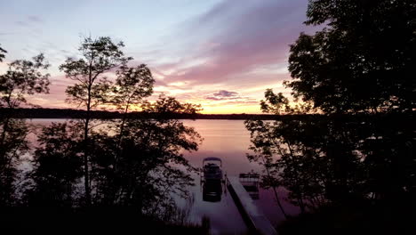 Flying-toward-docked-pontoon-boat-at-sunset-on-reflective-lake