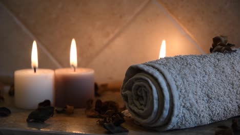 relaxing-spa-background-with-candles-with-flickering-flames,-some-wooden-petals-and-a-towel