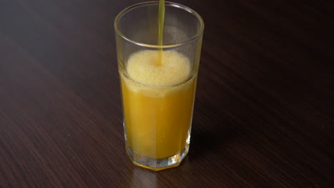 Gießen-Sie-Funkelnde-Orangenlimonade-In-Ein-Hohes-Glas-Auf-Einem-Holztisch