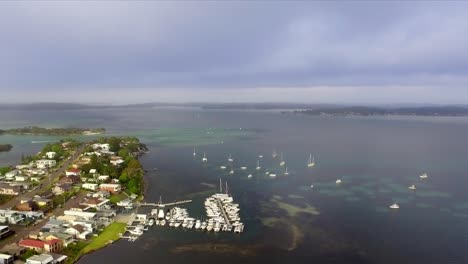 Aerial-drone-shot-flying-over-Lake-Macquarie,-Australia,-approaching-a-small-marina-and-looking-out-towards-islands-and-reefs
