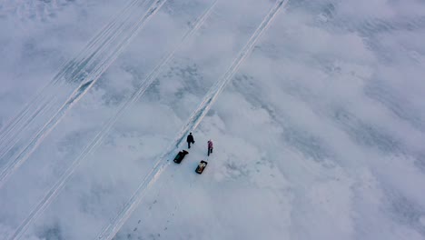 Aerial-top-down-over-two-ice-fishermen-pulling-tote-sleds-on-a-frozen-lake