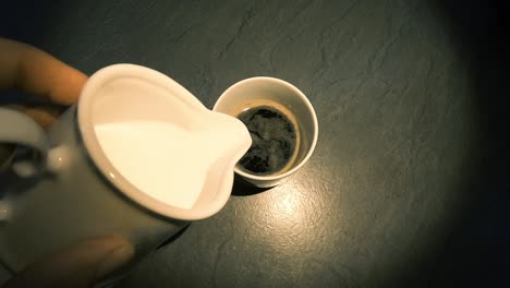 Hinzufügen-Von-Milch-Zum-Espressokaffee-Auf-Dem-Tisch-Mit-Mittellicht