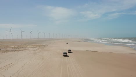 Pickup-trucks-driving-on-the-beach-towards-Atins,-bringing-kitesurfers-and-their-equipment
