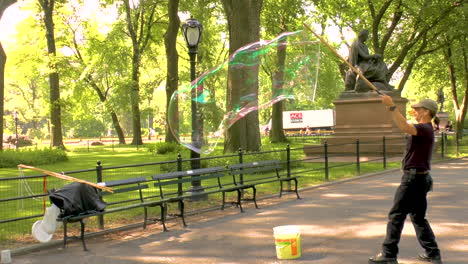 Man-blowing-large-soap-bubble-with-tri-strings-wand-in-the-air-while-performing-tricks-in-the-park