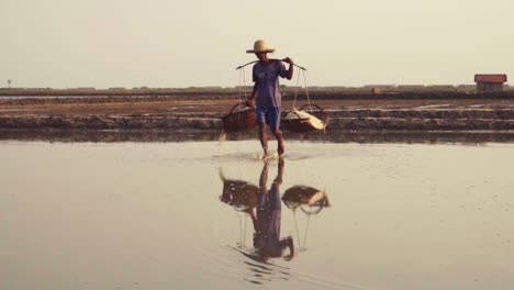 Slow-motion-of-worker-carrying-salt-baskets-dripping-with-water-on-the-reflective-salt-fields-of-Asia