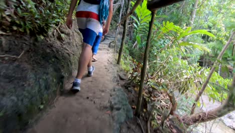 A-man-walking-down-a-path-then-turning-towards-a-beautiful-cascading-waterfall-in-the-tropical-jungle-environment-of-the-island-of-Bohol,-Philippines