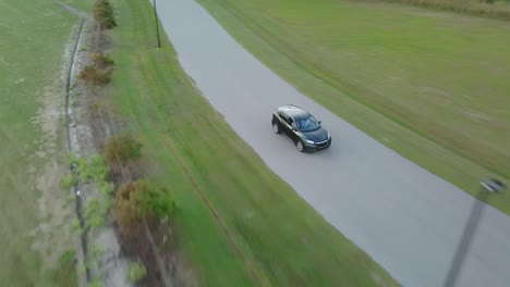 Aerial-View-of-Green-Crossover-Car-Driving-Away-on-Empty-Country-Road