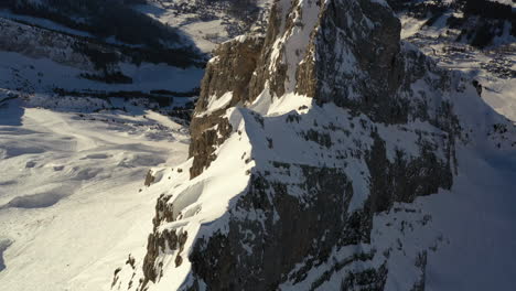 Aerial-view-flyng-over-a-mountain-ridge-with-mountains-in-the-background,-while-tilting-down-to-look-at-the-ridge-from-above-in-the-French-Alps-in-winter,-near-La-Clusaz