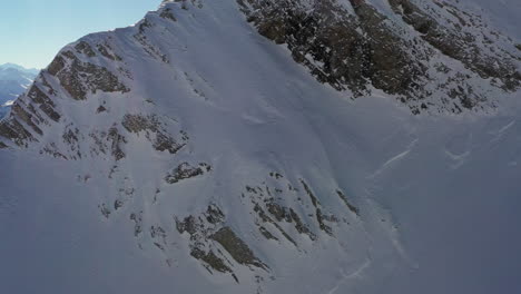 Aerial-view-of-a-right-to-left-pan-along-a-mountain-ridge-to-reveal-a-mountain-background-in-the-French-Alps-in-winter