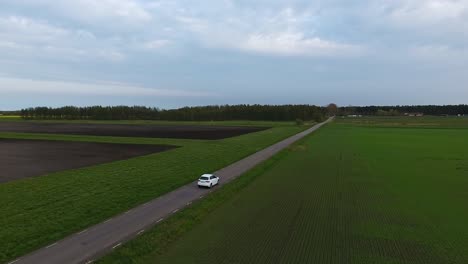 Extreme-Wide-Aerial-Drone-Shot-of-a-White-Car-Driving-on-a-Narrow-Country-Side-Road-in-South-Sweden-Skåne