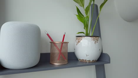 Panning-Right-Shot-of-an-Apple-HomePod-on-top-of-Modern-Looking-Bookshelf-adjacent-to-a-Pencil-Holder---Plant