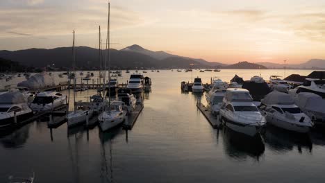 Drone-fliyng-among-yachts,-boats-and-sailboats-anchored-at-a-marina-with-a-beautiful-sunset