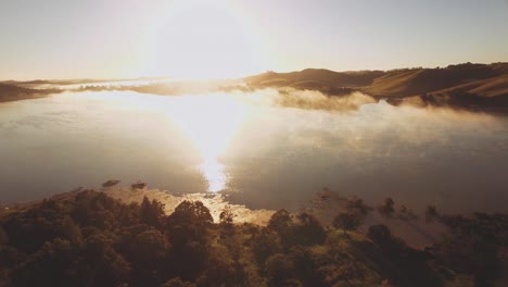 Luftaufnahme-über-Einem-Wald-Und-See,-Der-Im-Ersten-Morgenlicht-Mit-Nebel-Bedeckt-Ist