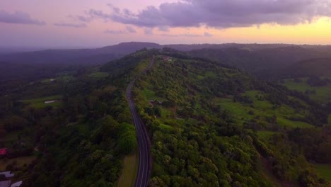 Aerial-view-of-a-road-with-cars-through-tropical-forest-valley-at-sunset