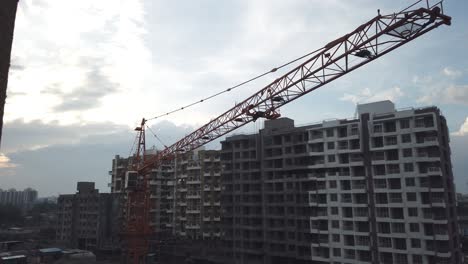 A-Crane-Panned-Across-at-a-Construction-Site-during-a-Cloudy-Evening-with-Residential-Complexes-and-Traffic-on-Street