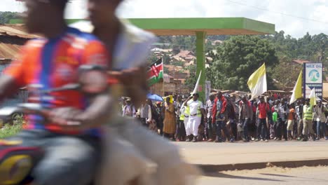 Una-Toma-Amplia-De-Un-Gran-Grupo-De-Católicos-Kenianos-Caminando-Con-Una-Escolta-Policial-Por-Una-Concurrida-Carretera-De-Uganda-Durante-Una-Peregrinación-Espiritual.