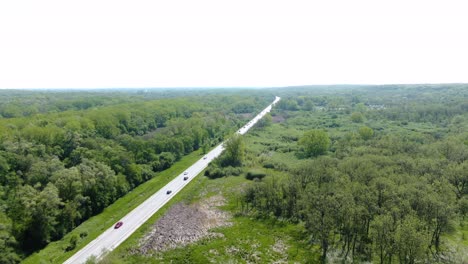 Aerial-shot-of-a-rural-road-going-through-a-thick-forest-in-the-plains