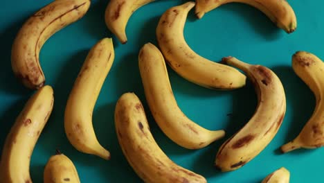 Una-Toma-Macro-De-Plátanos-Orgánicos-Amarillos-Maduros-Girando-Sobre-Un-Fondo-Azul
