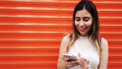 Zeitlupe:-Schönes-Junges-Mädchen-Benutzt-Smartphone-Vor-Orangefarbenem,-Rotem-Hintergrund