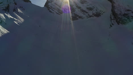 Pan-up-to-reveal-snow-covered-mountain-ridge-with-sun-behind-with-sun-flare,-in-the-French-Alps-in-winter