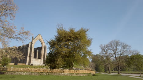 Establishing-Shot-revealing-Bolton-Abbey-Ruins-on-a-Beautiful-Sunny-Summer’s-Morning-in-Yorkshire,-England-with-Lone-Bird-Flying-through-Frame