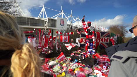 People-pay-their-respects-at-the-Gordon-Banks-statue-by-the-Stoke-City-stadium,-people-signing-shirts,-scarves,-flags-and-the-book-of-remembrance
