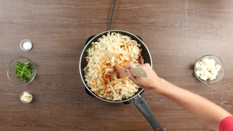 Top-down-shot-of-combining-fusilli-pasta-with-tomato-sauce-in-large-pan,-using-wooden-spatula