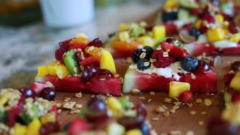 Panning-Shot-over-slices-of-watermelon-with-a-yogurt-cream-on-top-along-with-granola-and-a-variety-of-fruits-including-blueberries,-pineapple,-strawberries,-and-raspberries