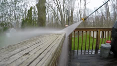 A-man-uses-a-power-washer-to-clean-a-wooden-deck-railing-post