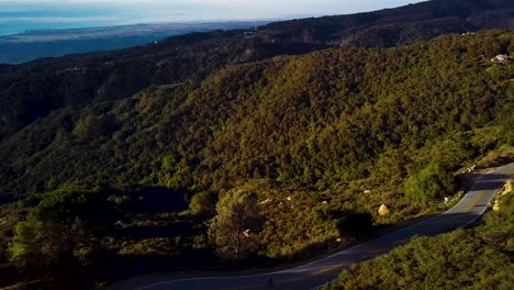 Cyclist-rides-tight-turn-of-California-Mountain-Road-at-Dawn,-Drone-Chase