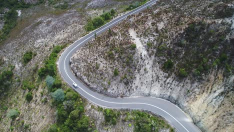 Aerial-shot-of-a-car-driving-on-a-windy-road-in-Tasmania,-Australia
