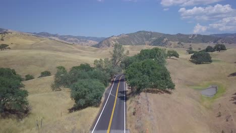 4K-drone-shot-moving-forward-down-country-road-lifting-to-reveal-beautiful-landscape-turns-right-to-show-curving-road-winding-through-California-rural-fields,-stretching-out-as-far-as-eye-can-see