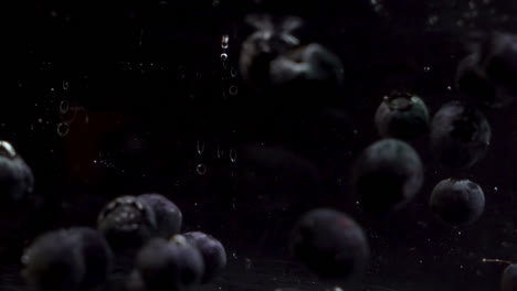 Blueberries-Floating-Into-Water-On-Black-Background