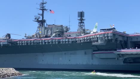 Two-jet-skis-passing-by-the-USS-Midway-Museum,-a-historic-US-naval-aircraft-carrier-museum-located-in-downtown-San-Diego,-California-at-Navy-Pier