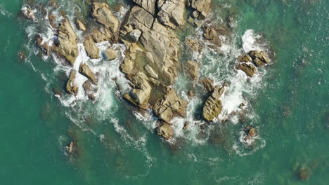 Top-down-view-of-sea-waves-and-fantastic-rocky-coast,-Praia-Armacao,-Florianopolis,-Santa-Catarina,-Brazil