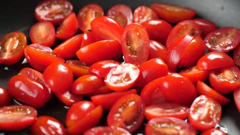 Close-up-shot-in-slow-motion-of-heated-large-pan-with-olive-oil-and-putting-halved-cherry-tomatoes-in