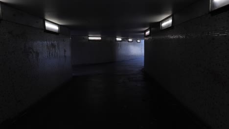 Handheld-footage-of-person-walking-scared-through-dim-lit-underpass-towards-light-at-end-of-tunnel-with-person-coming-towards