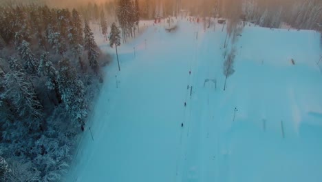 Hochschwenkbare-Luftaufnahme-Eines-Von-Tannenbäumen-Umgebenen-Snowboard-Geländeparks-Bei-Sonnenuntergang