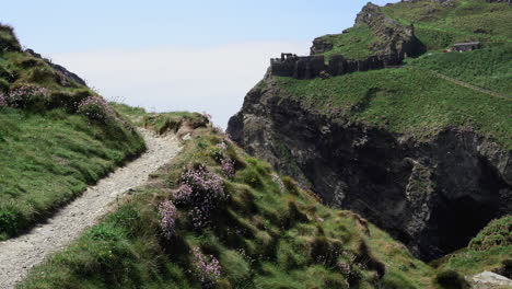 Tourist-on-vacation-walking-on-top-of-a-cliff-along-the-path-that-leads-to-the-ruins-of-Tintagel-castle-in-Cornwall