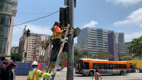 A-professional-repair-man-on-a-portable-ladder-using-tools-to-fix-a-broken-traffic-signal-light-on-the-busy-intersection-of-Pershing-Square-in-downtown-Los-Angeles