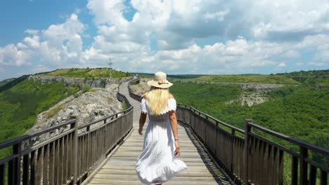 Woman-in-white-dress-and-a-sun-hat-opens-gate-doors,-walks-on-bridge