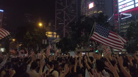 Wide-Shot-Tilt-Up-protesters-waving-US-flags-in-Hong-Kong,-city-background