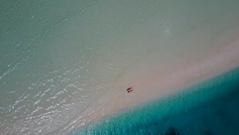 Ein-Paar-Liegt-Mit-Dem-Gesicht-Nach-Unten-Am-Wunderschönen-Weißen-Sandstrand-Der-Malediven,-Während-Die-Kühlen-Wellen-Vorbeirauschen-–-Luftaufnahme