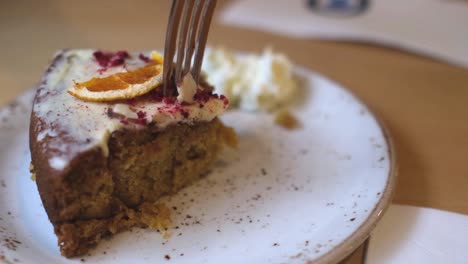Close-Up-Of-Woman-Eating-Slice-Of-Zesty-Lemon-Carrot-Cake-with-fork-and-cream-on-a-plate,-slow-motion