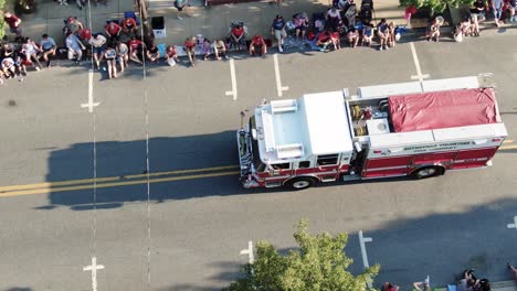 Aerial-turn-and-top-down-shot-of-fire-truck-in-Fourth-of-July-parade,-crowds-line-streets