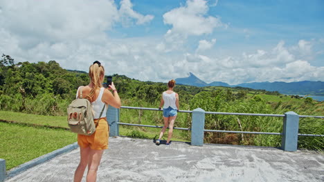 Blonde-girl-taking-picture-of-friend-with-Volcano-View,-Arenal,-Costa-Rica