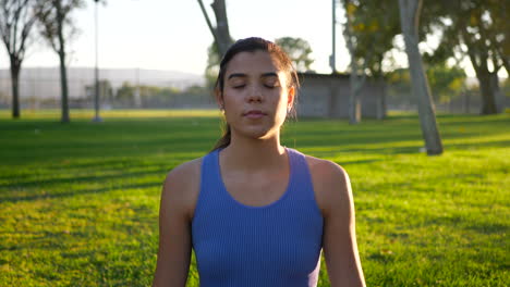 A-beautiful-young-woman-yogi-sitting-on-a-yoga-mat-in-calming-meditation-in-the-park-at-sunrise