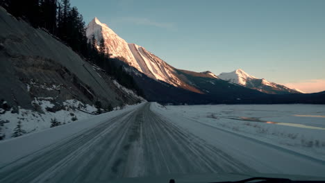 Toma-De-Punto-De-Vista-Conduciendo-A-Lo-Largo-De-Un-Camino-Cubierto-De-Nieve-Con-Una-Montaña-Dramática-En-La-Distancia