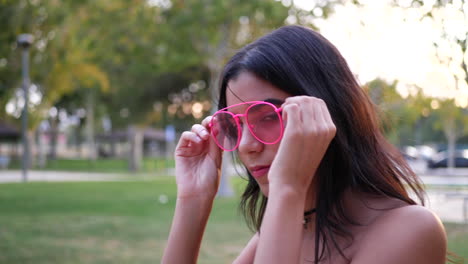 A-young-hispanic-woman-hipster-wearing-vintage-fashion-clothing-and-retro-pink-aviator-sunglasses-in-a-park-playground-SLOW-MOTION